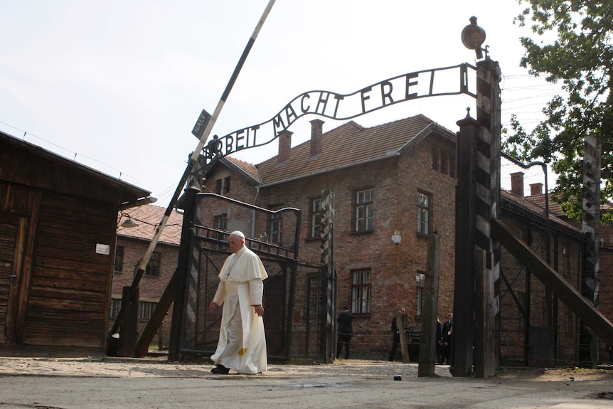Pope Francis walks through a gate with the words "Arbeit Macht Frei"