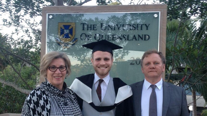 a woman, a young man and an older man standing in front of a university sign