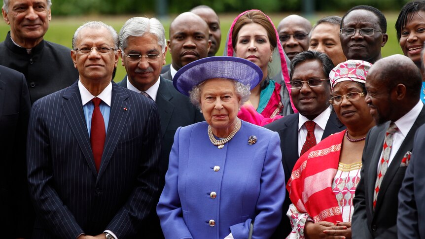queen in purple in the centre closely surrounded by men and women leaders in suits and national dress