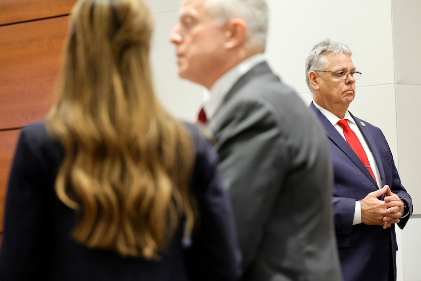 Scot Peterson stands in a suit in a courtroom in Fort Lauderdale near two other people in suits