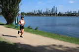 A woman jogs along a path with Melbourne's city skyline in the background.