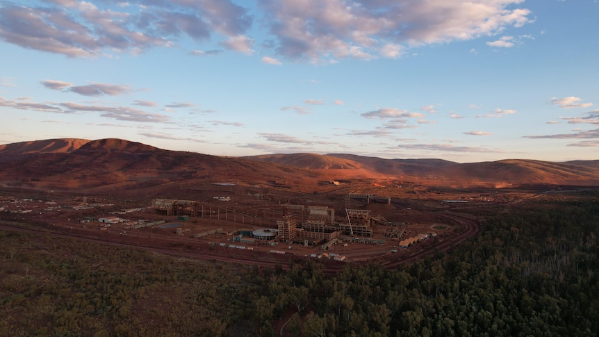 red dirt mine site with hills in background and trees around, blue skies