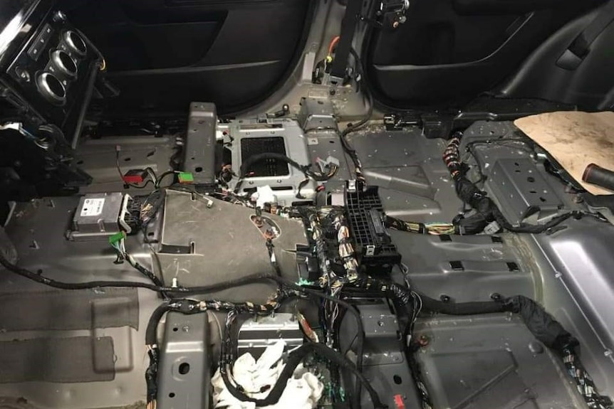 The interior of a car with the seats and trim removed, revealing wiring and electronics.