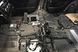 The interior of a car with the seats and trim removed, revealing wiring and electronics.