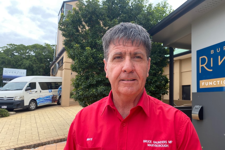 Older man wearing a red long sleaved shirt with his name embroided on it. He seems distracted