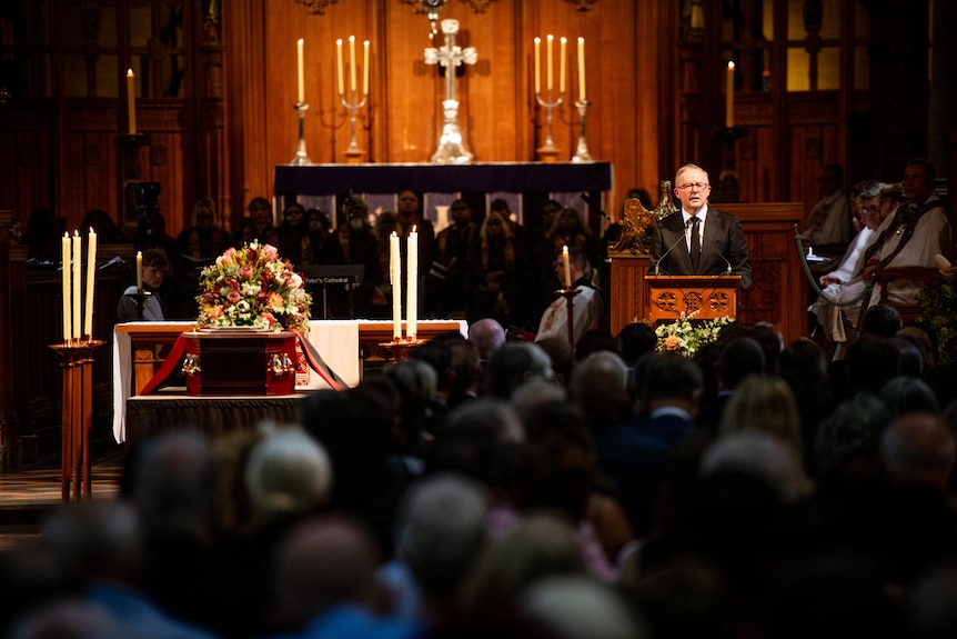 Anthony Albanese speaks at a lecturn next to a coffin adorned with flowers in front of mourner inside a cathedral