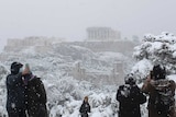 People take pictures in front of the ancient Acropolis hill during a snowfall.