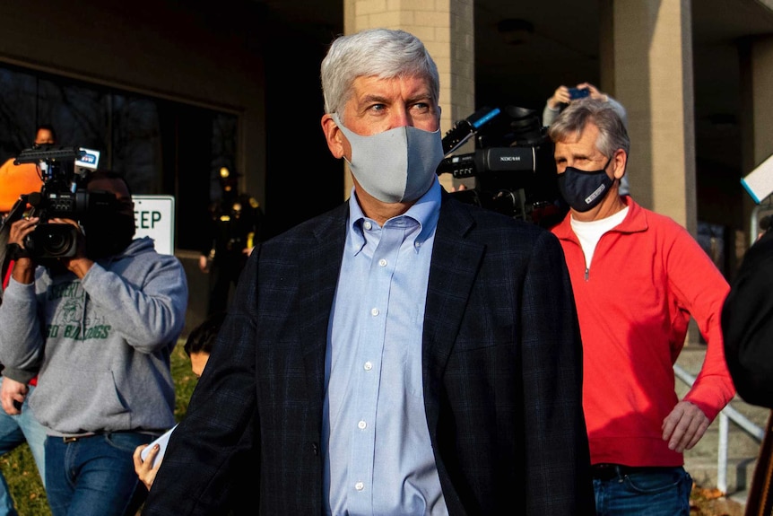 Former Governor Rick Snyder walks past the media wearing a face mask.