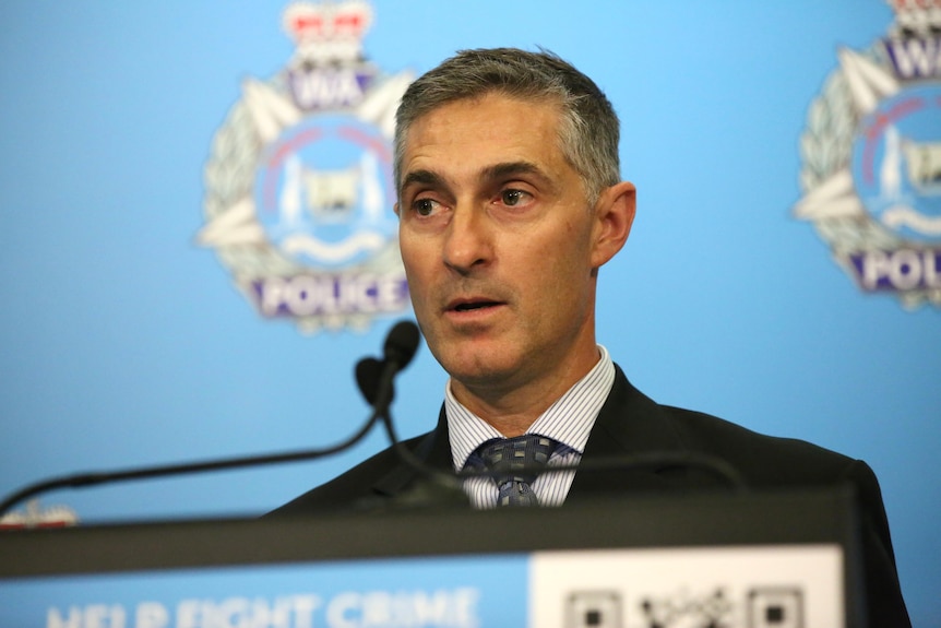 A man in a suit and tie looking serious at a lectern.