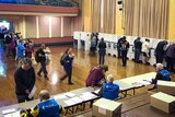 Polling booth in a town hall, people standing in a queue to register, others making their vote in cubicles