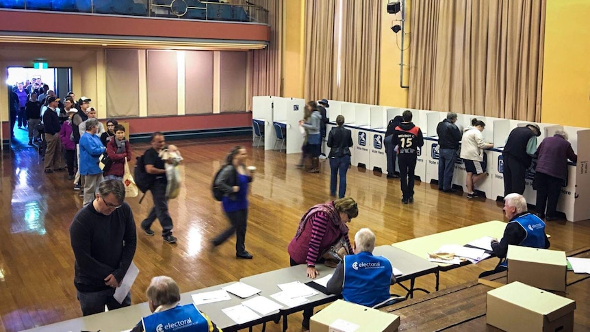 Polling booth in a town hall, people standing in a queue to register, others making their vote in cubicles