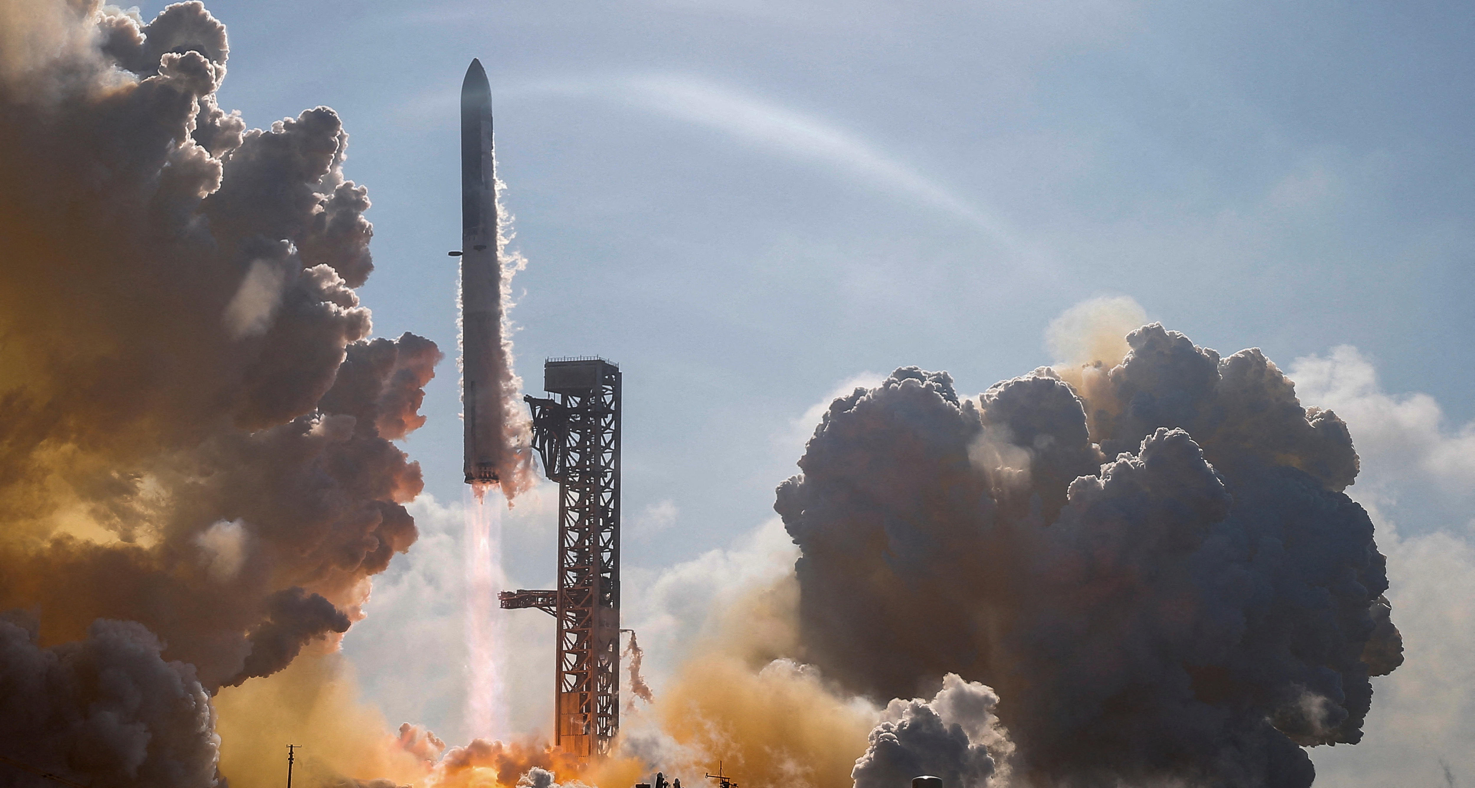 A white rocket launches into the sky on a clear day, with grey and yellow clouds billowing below.