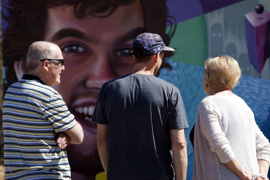 A younger man chats with two older people. All three have their backs to the camera