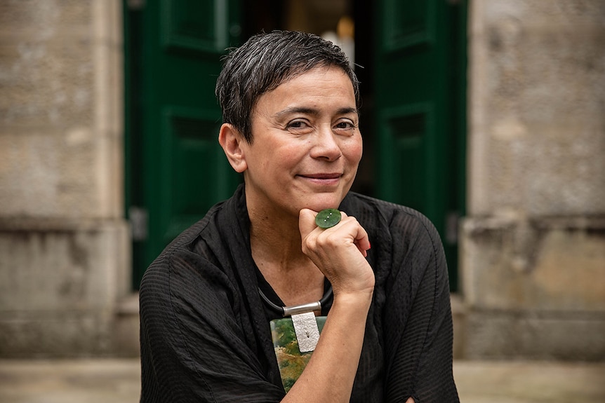 Colour close-up photo of artist Lisa Reihana posing in front of sandstone building at the National Art School in Sydney.