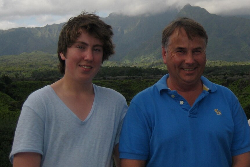 A father and two sons smile in front of a mountain.