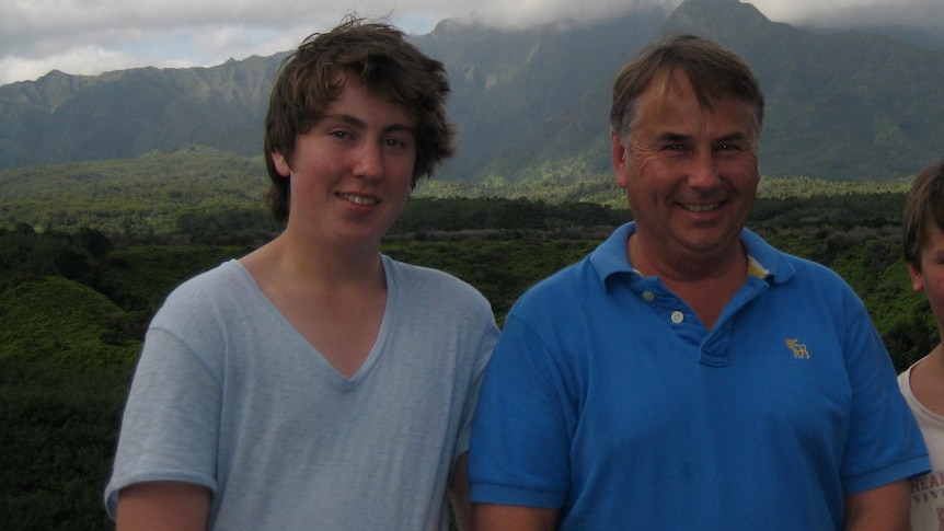 A father and two sons smile in front of a mountain.