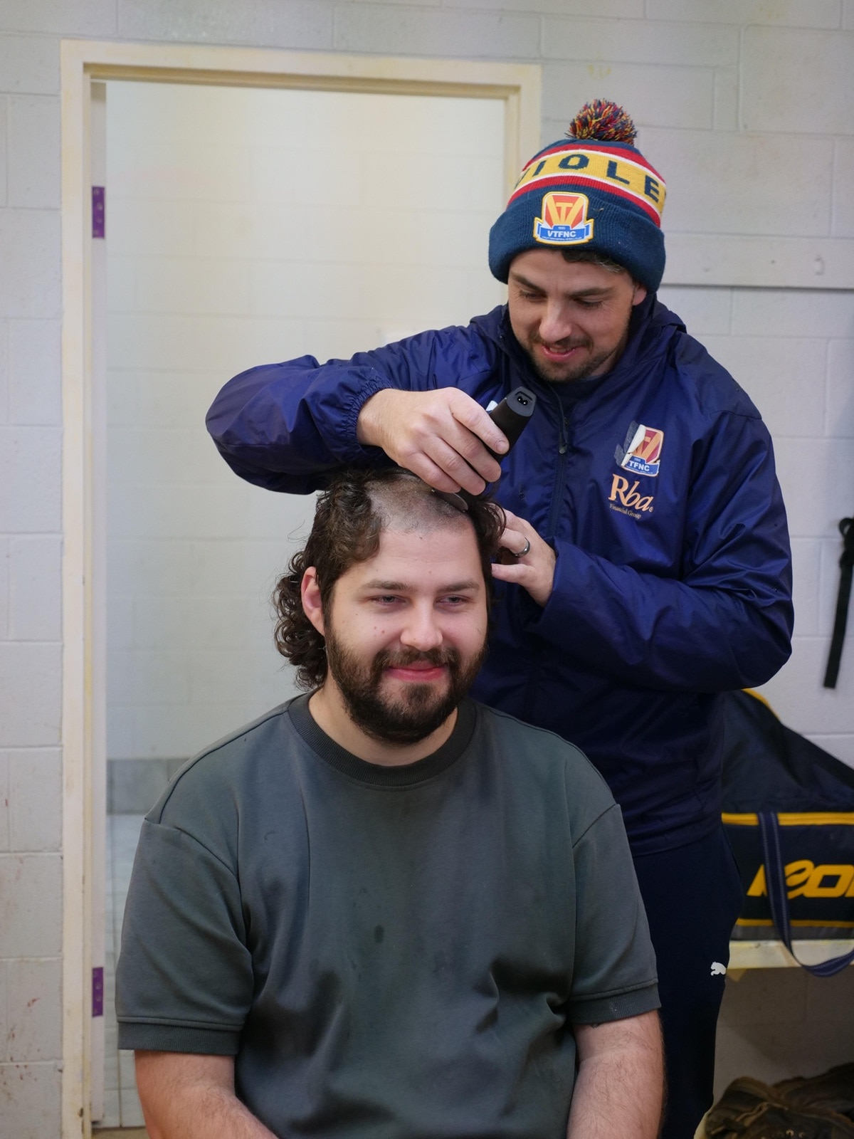 One man shaves the head of another in the dressing room