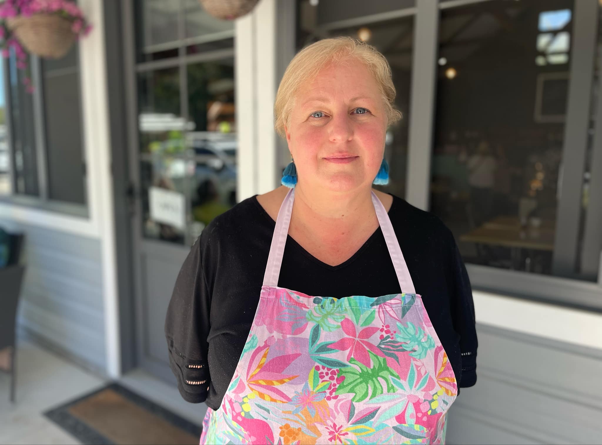 A woman with an apron on smiles at the camera.