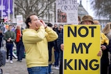 Man in a yellow hoodie standing next to a protester holding a sign shouting.