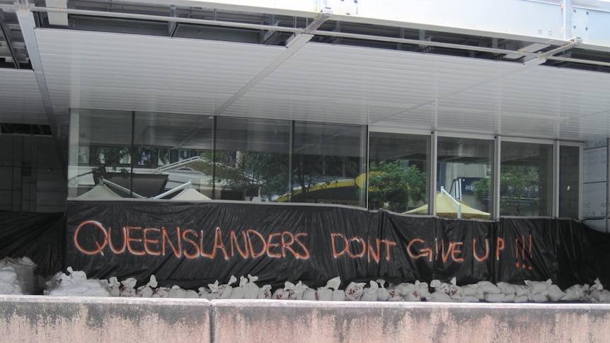 Sign reading 'Queenslanders don't give up!' hangs across the front of a building in Brisbane's CBD