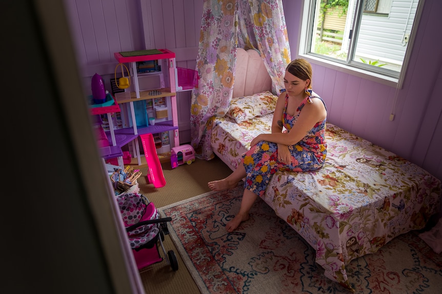 A woman in a colourful dress sits on a small child's bed 