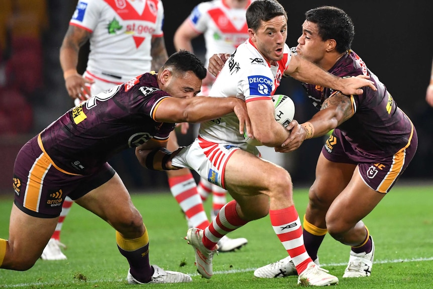 Ben Hunt holds the ball under his right arm as he is tackled by two players wearing maroon