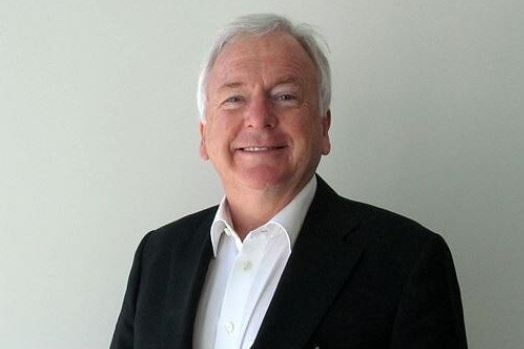 A man with white hair and a black suit jacket, smiling