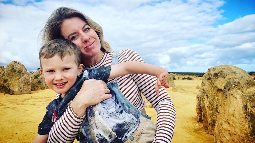 A blonde haired mother holding her young son in front of rocks