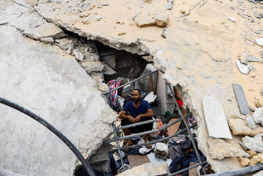 A Palestinian man sits amidst the rubble at the site of Israeli strikes on houses,