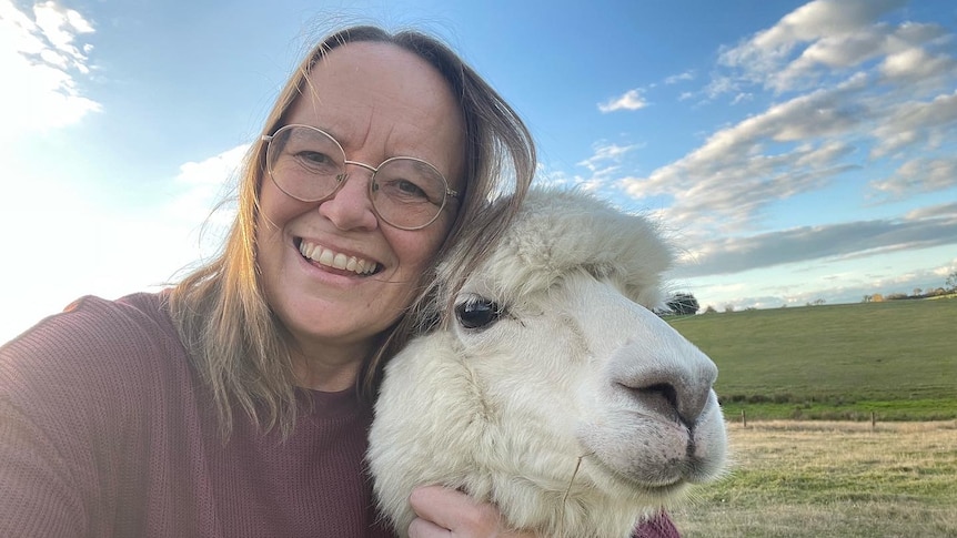Angela Betheras smiling and cuddling an alpaca