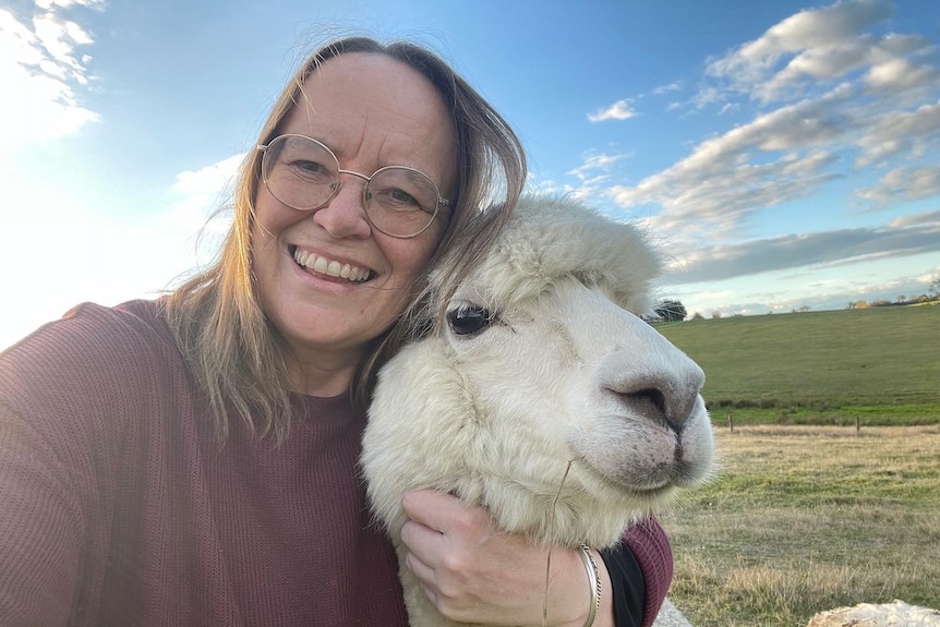 Angela Betheras smiling and cuddling an alpaca