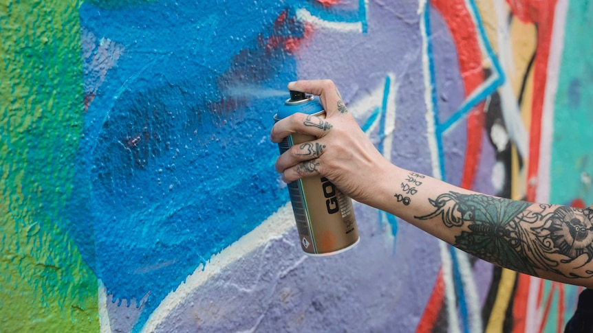 A hand holding a spray can near a colourful wall