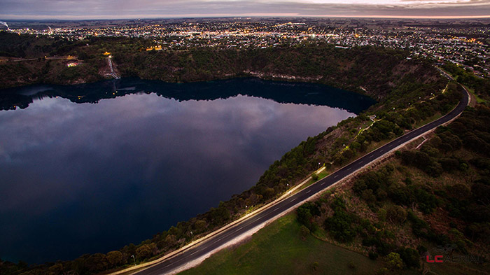 An aerial view of a dark blue lake with a sunset sky reflected in the water.
