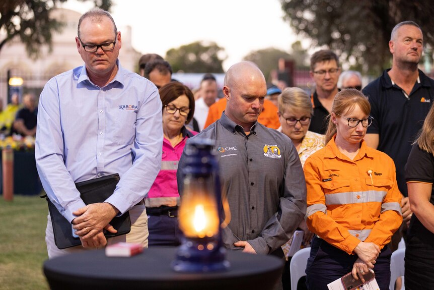 A miner's lantern burning with a flame of remembrance as a crowd pauses for a minute's silence. 