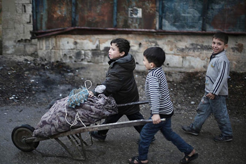 Children push a small wheelbarrow with firewood wrapped in a cloth bag.