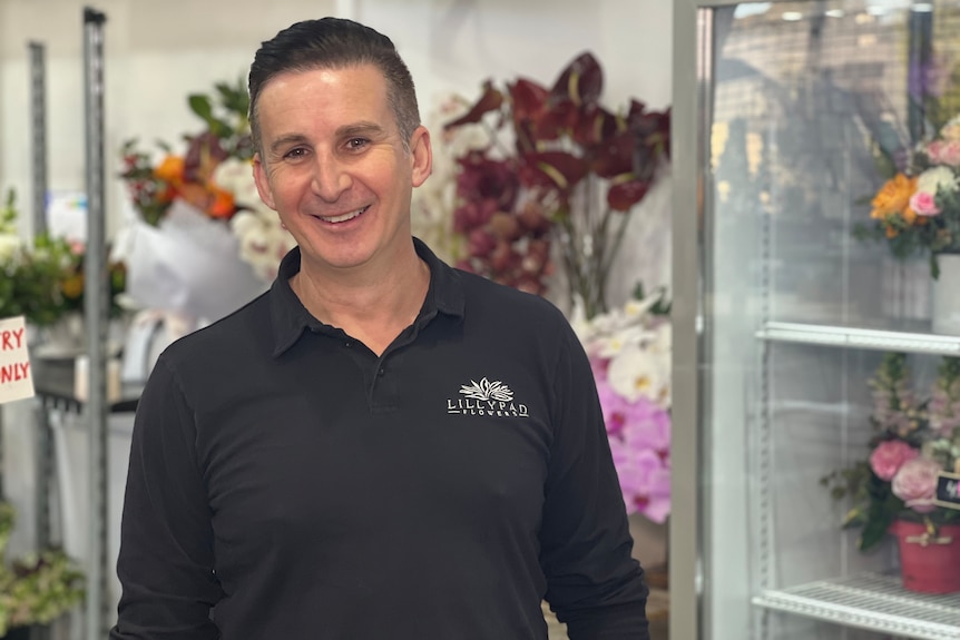 A man wearing a long sleeved collared black polo shirt standing in a florist.