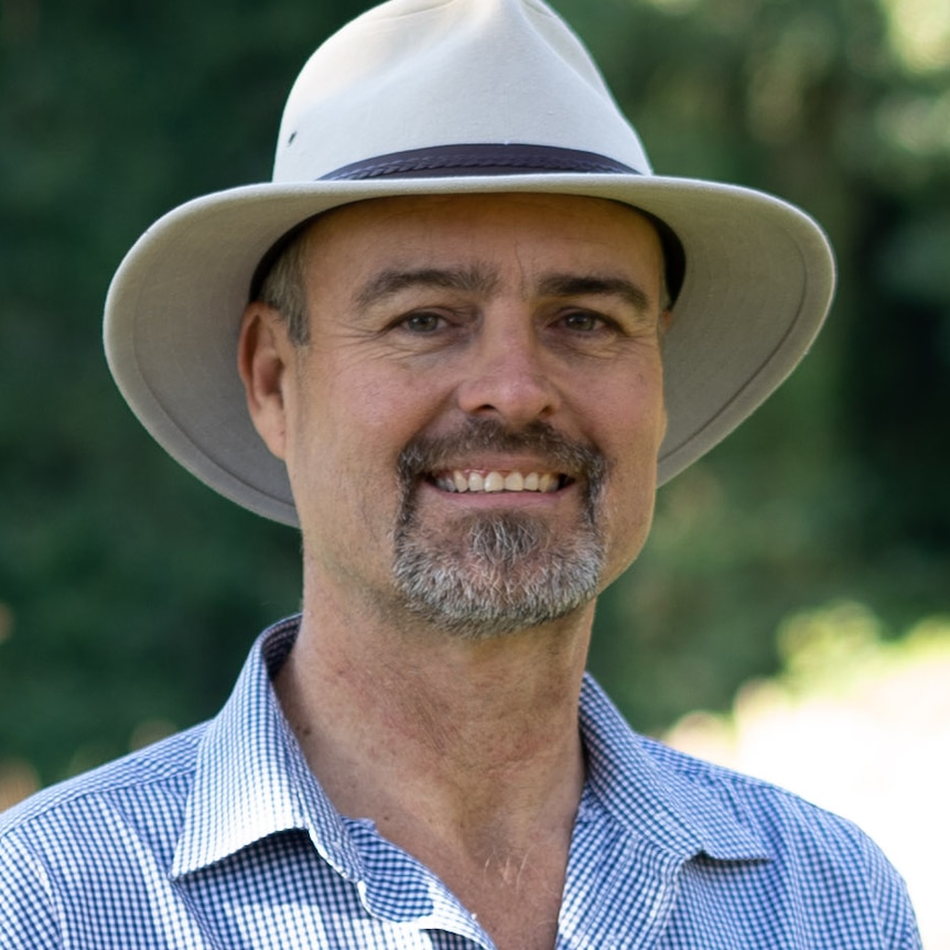 A man in a blue shirt and a wide brim hat smiles