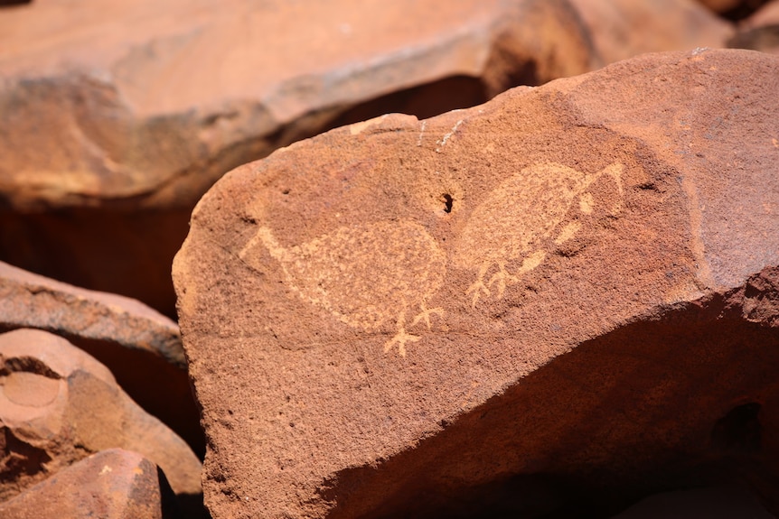 A close up on a red rock that has been carved with the images of birds.