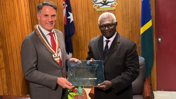 Richard Marles with short grey hair wearing grey suit holds a plaque with Manasseh Sogavare in a black suit