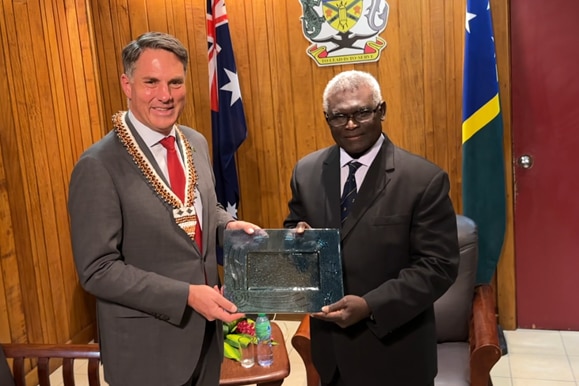 Richard Marles with short grey hair wearing grey suit holds a plaque with Manasseh Sogavare in a black suit