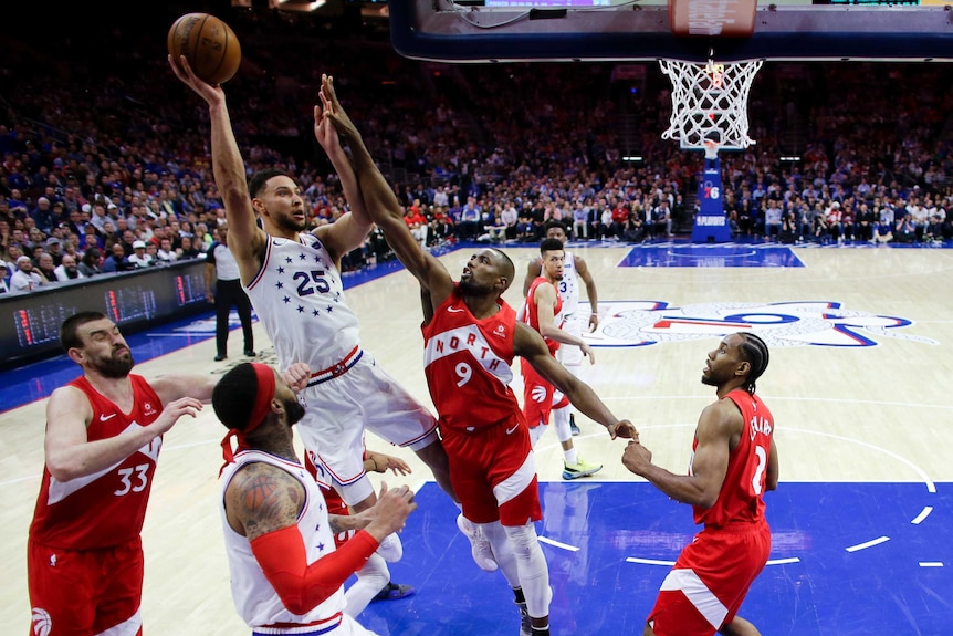 Basketballer leans back to shoot for a basket as several opponents try to block him.