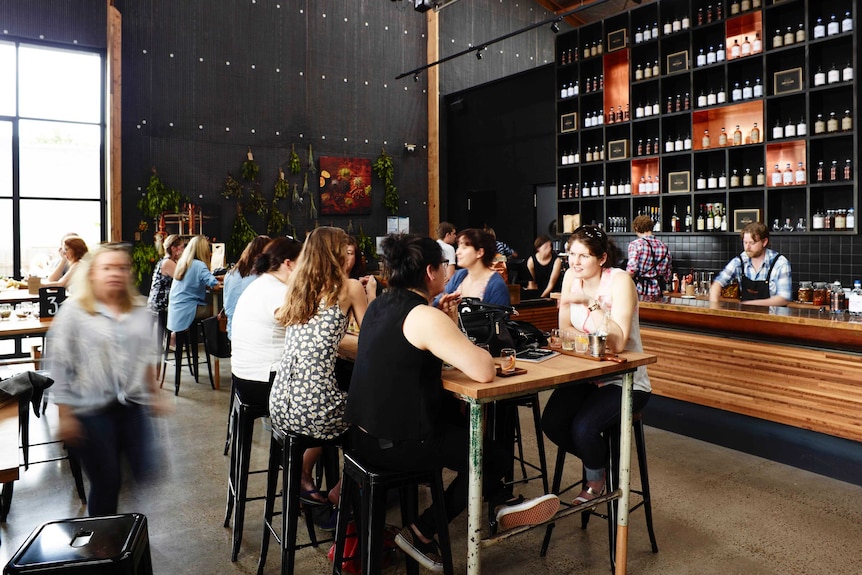 People sit at tables drinking in a large room lined with bottles of gin, Four Pillars in Yarra Valley Victoria