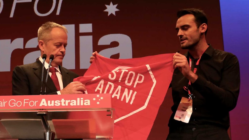 Mr Shorten is holding the banner the protester is brandishing, which says "Stop Adani"