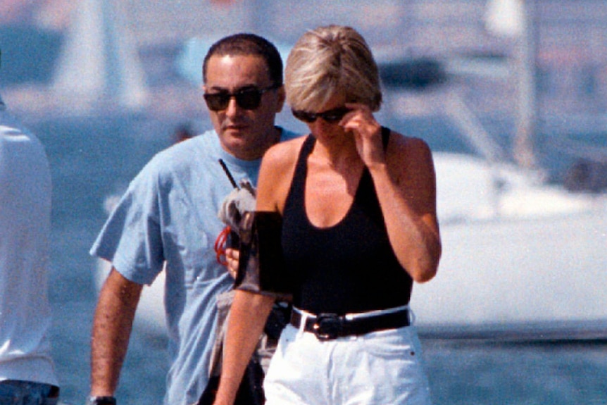 Dodi and Diana walking along a harbour in summer clothes and sunglasses.
