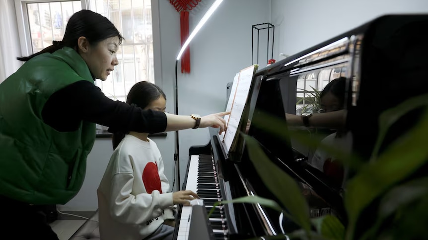 A female piano teacher conducts a lesson for a female student inside a classroom