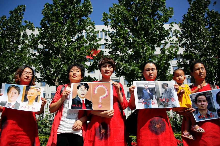 A group of Chinese women in red hold photos of their husbands. 