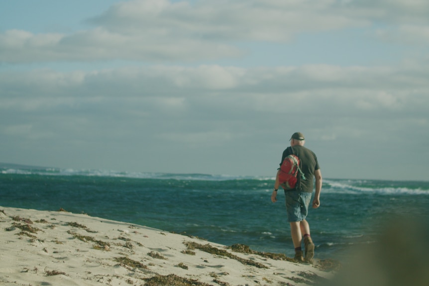 Man walks along beach wearing backpack