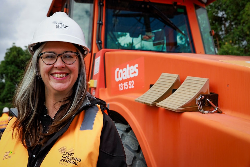 A woman smiling at the camera wearing a hard hat and hi vis standing in front of a truck.