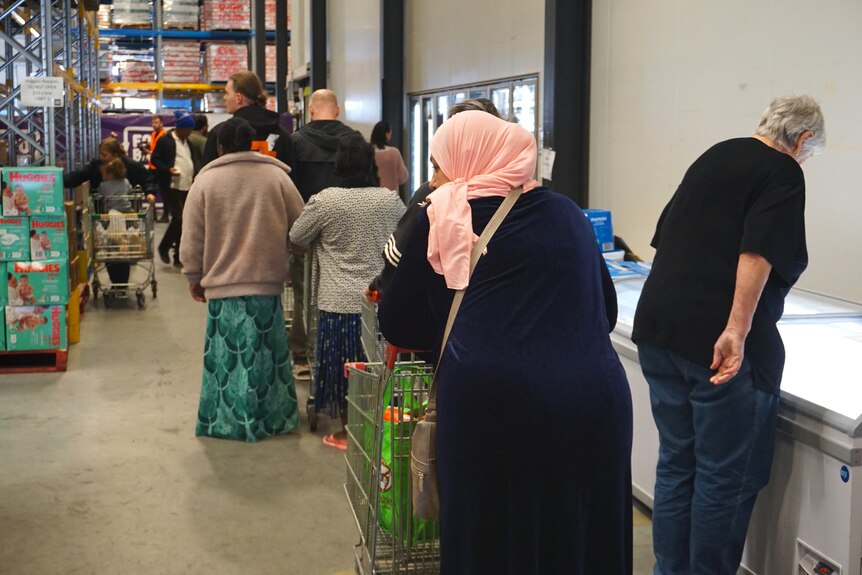 A queue of shoppers line up with trolleys and groceries in a checkout queue inside Foodbank WA's Perth depot.