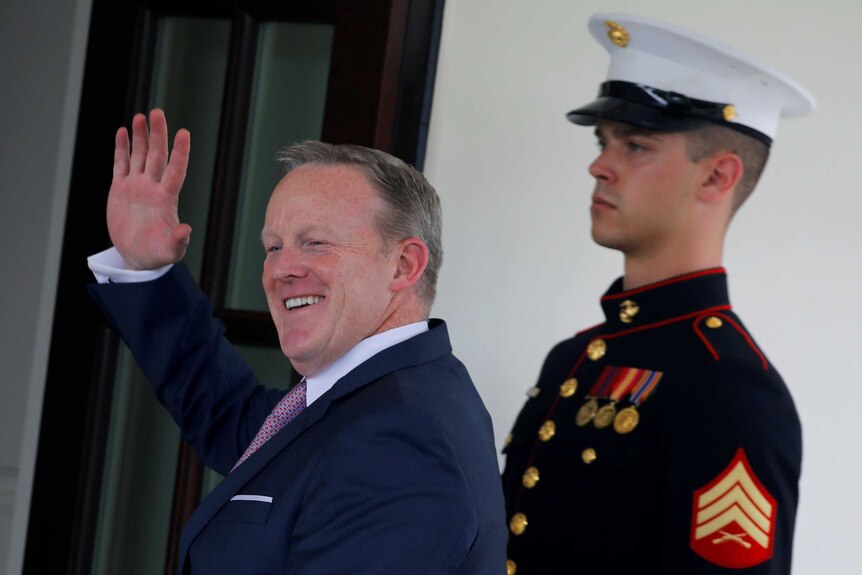 White House Press secretary Sean Spicer waves as he walks into the White House, soldier behind him